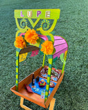 A colorful Day of the Dead themed altar made of MDF, featuring a vibrant trajinera with decorations and the name 'Lupé' on top.