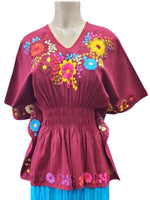 Mannequin wearing a pink top with floral embroidery and blue skirt on a white background