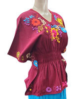 Mannequin wearing a red top with colorful floral embroidery and a blue skirt on a white background